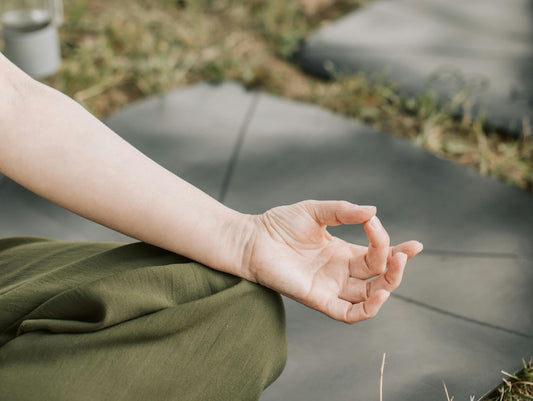 Hand im Meditations-Mudra auf dem Knie abgelegt, Yogamatte und Wiese im Hintergrund