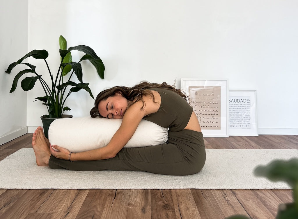 Frau in einer Vorbeuge mit Yogabolster zwischen den Beinen